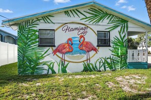 Een gebouw met een muurschildering van flamingo's en palmbladeren, met de tekst 'Flamingo Cove'.
