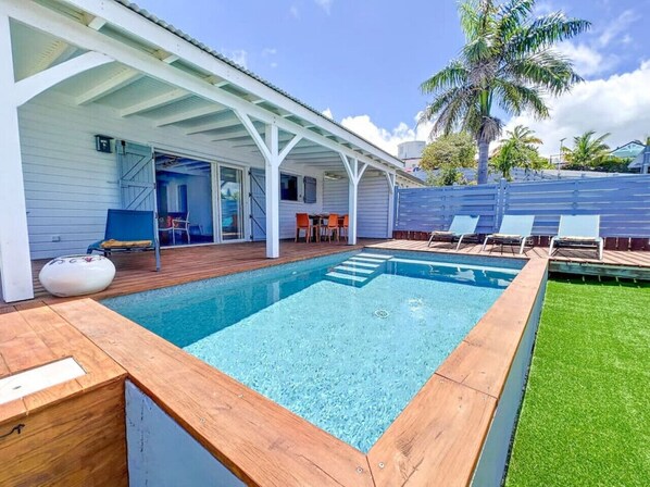 A rectangular swimming pool with a wooden deck and a covered patio area.