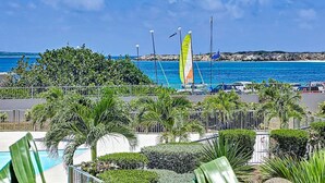 Une vue sur la côte, avec une piscine, des palmiers et un voilier arborant des drapeaux.