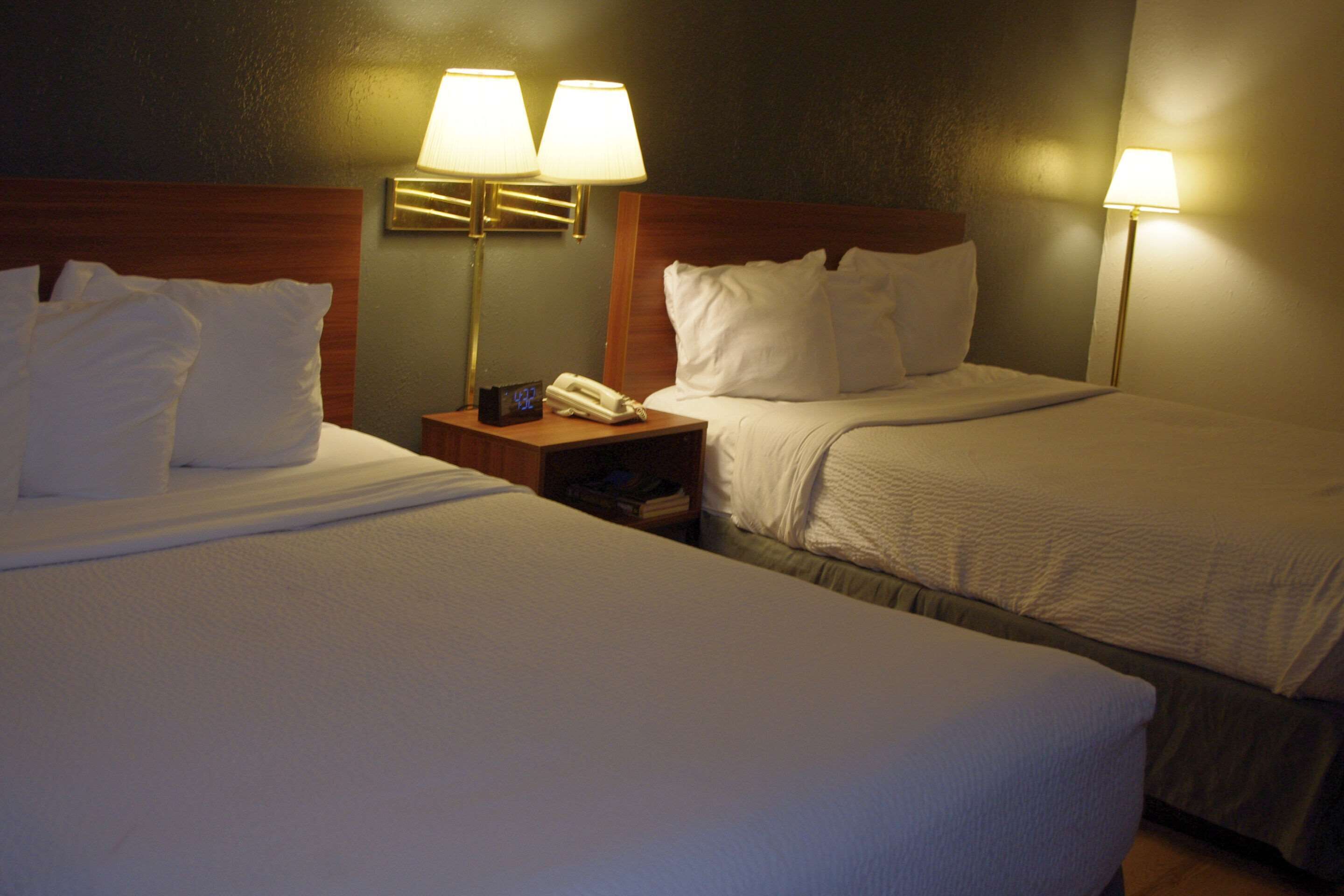 Two single beds with white linens, wooden headboards, bedside tables with lamps, and a small clock.
