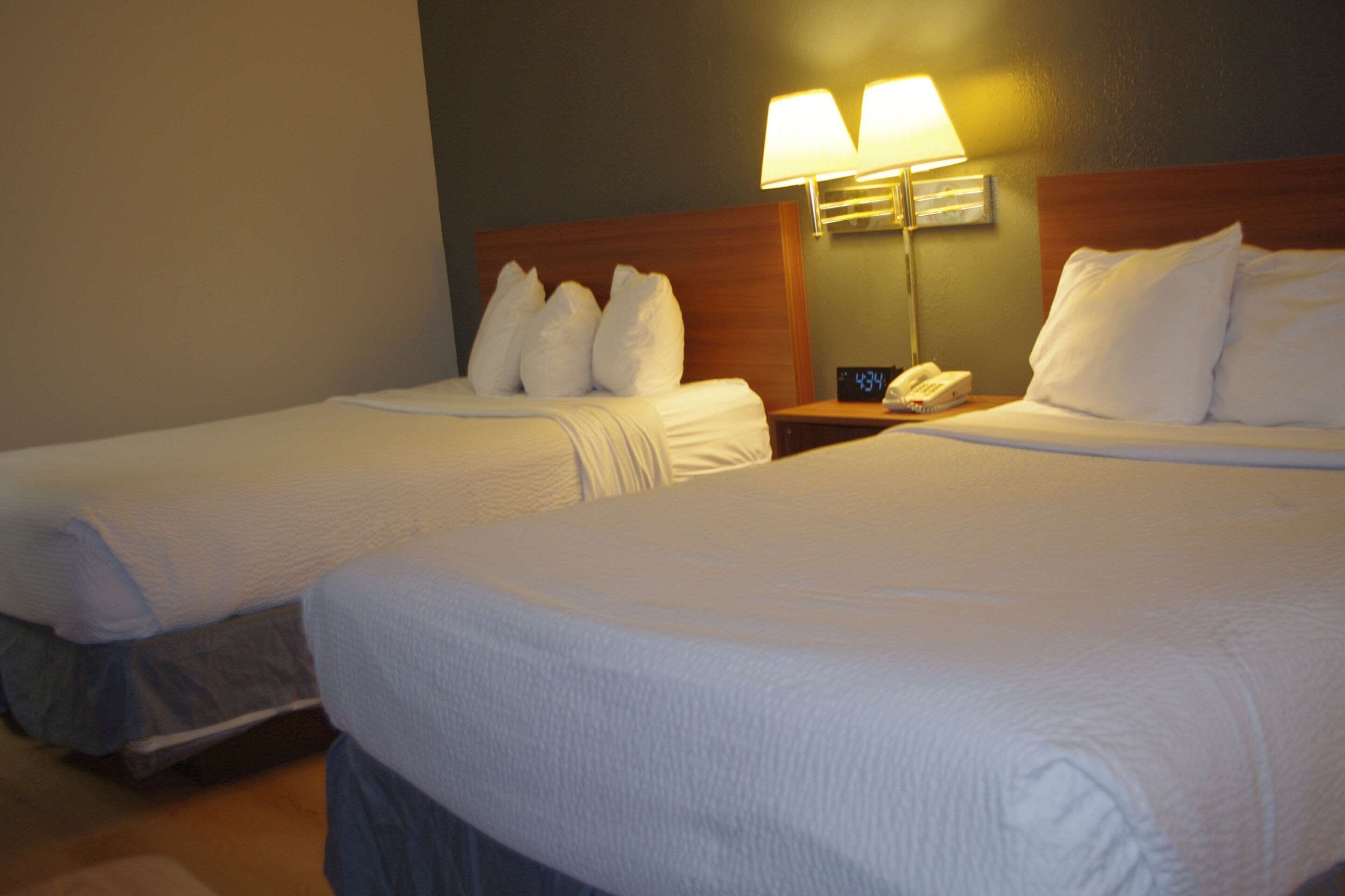 Two single beds with white bedding, a nightstand with a lamp, and a clock displaying 4:34.