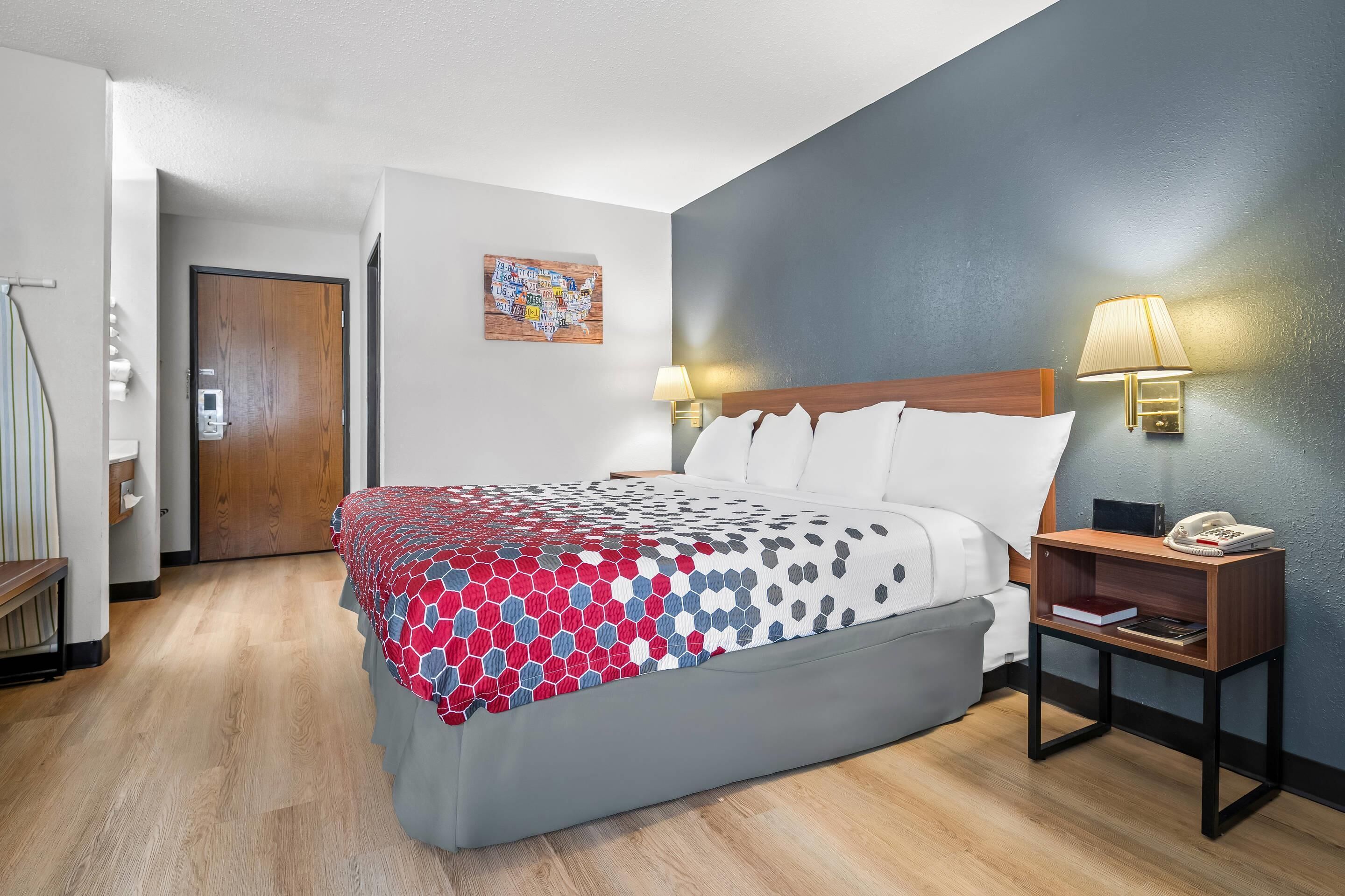 A hotel room with a bed, bedside tables, a lamp, a map artwork, and a door.