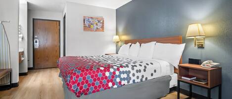 A hotel room with a bed, bedside tables, a lamp, a map artwork, and a door.