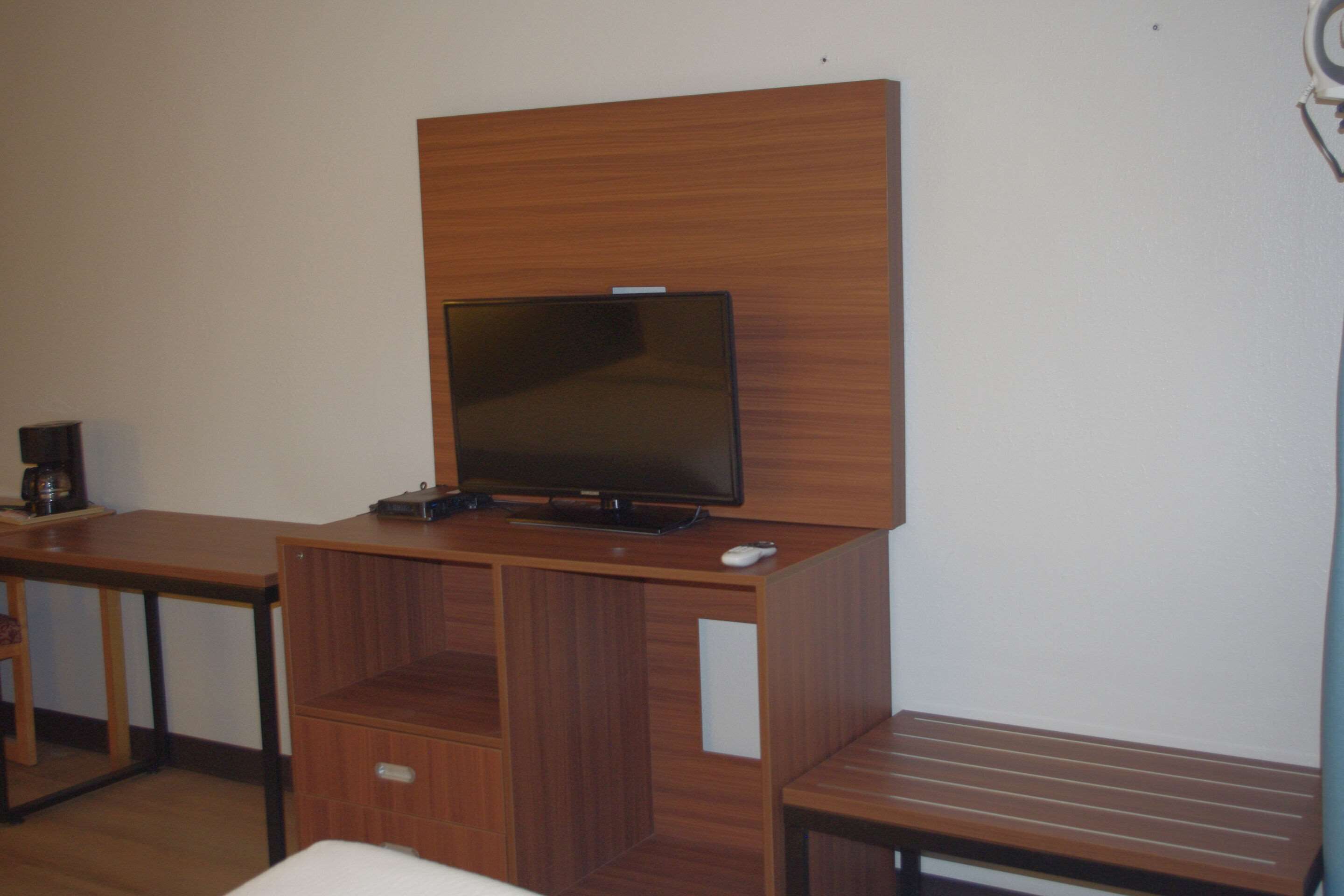 Habitación con un mueble de televisión de madera, un televisor de pantalla plana, una cafetera y una mesita.