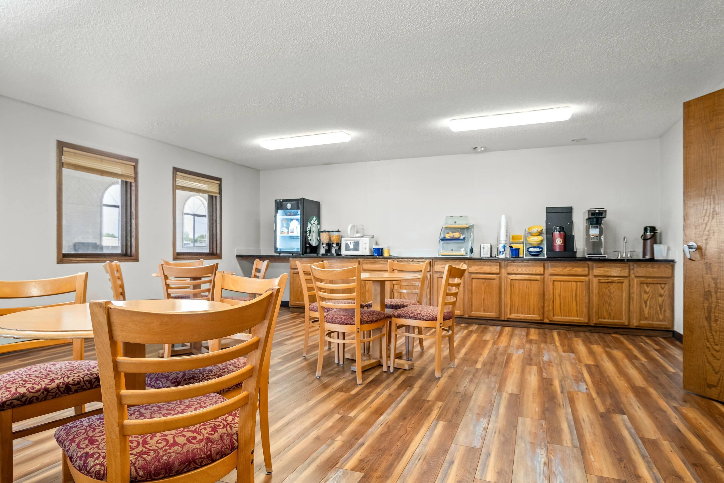 A dining area with wooden chairs and tables, a kitchen with appliances, and a wooden floor.