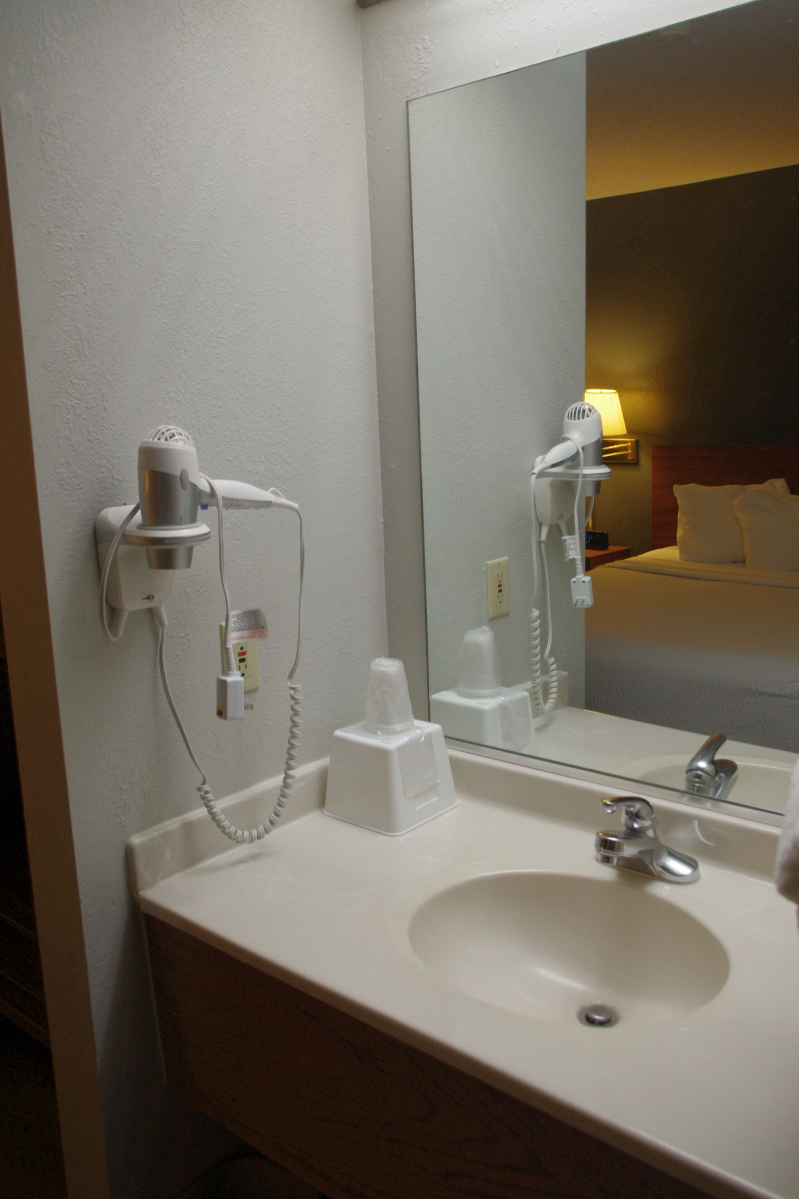 Un baño de hotel con lavamanos, espejo y secador de pelo fijado en la pared.