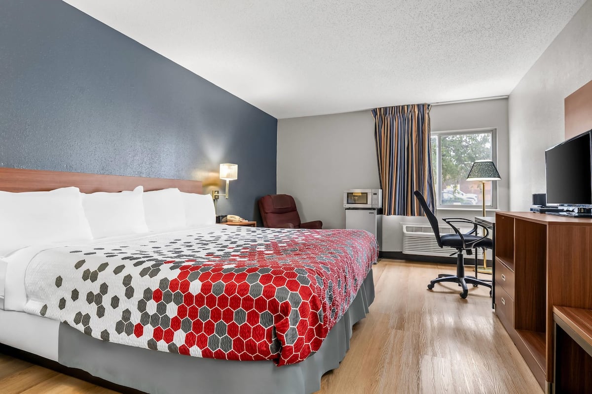 Una habitación de hotel con cama, escritorio, silla, televisor y ventana con cortinas.