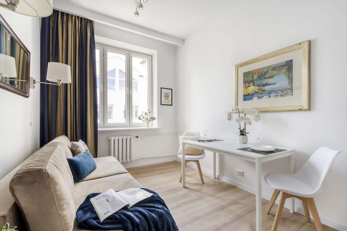 A modern living room with a sofa, a dining table with chairs, a radiator, and a window with curtains.