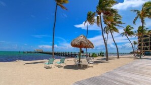 A beach with lounge chairs, a wooden deck, and palm trees.