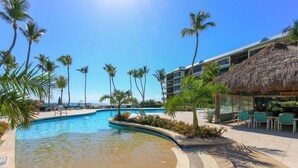A resort pool area with palm trees, a thatched-roof structure, and a clear blue sky. - Direct Oceanfront with private staircase to beach prestigious Islamorada CondoComplex (Islamorada)