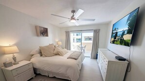 Une chambre à coucher comprenant un lit, des tables de chevet, une commode, un ventilateur de plafond, un téléviseur et une vue sur l’extérieur.