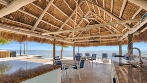 Une terrasse au bord de la plage, dotée d’un toit de chaume, de sièges extérieurs et offrant une vue sur la mer.