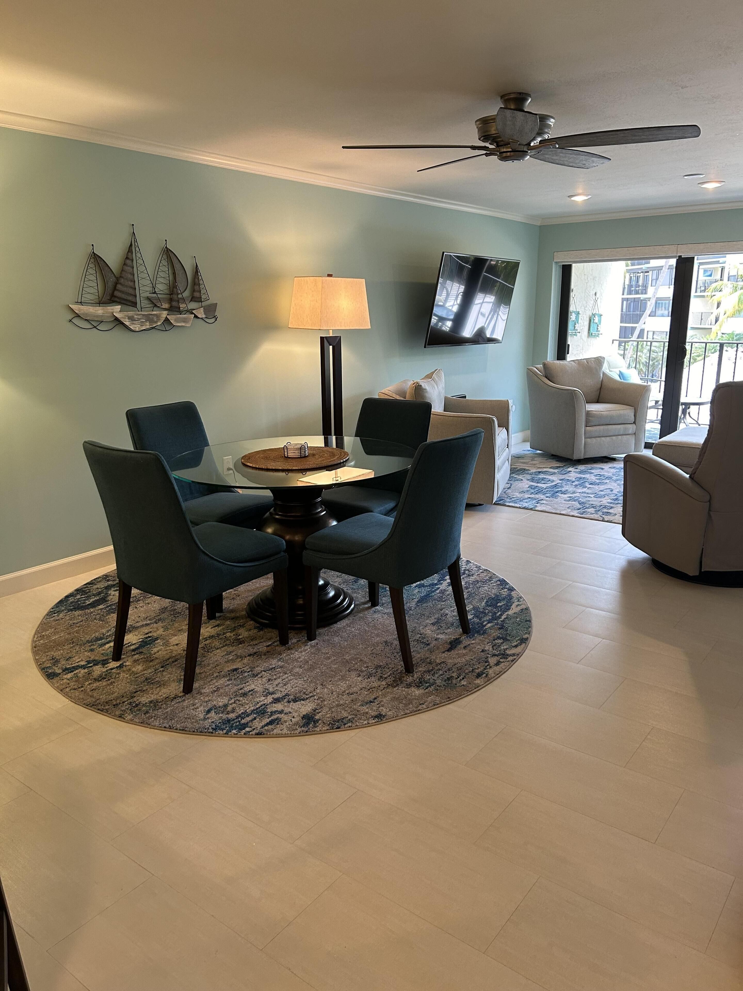 Un coin repas avec une table ronde, quatre chaises, une lampe et un ventilateur de plafond.