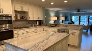 A kitchen with white cabinets, a marble countertop, stainless steel appliances, and a view to the living area. - This condo is located in one of Islamorada's most prestigious condo complexes. (Islamorada)