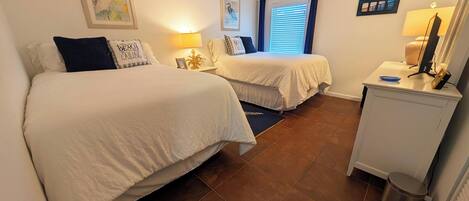 Camera d'albergo con due letti, una scrivania con lampada, un cestino e quadri appesi alla parete.
