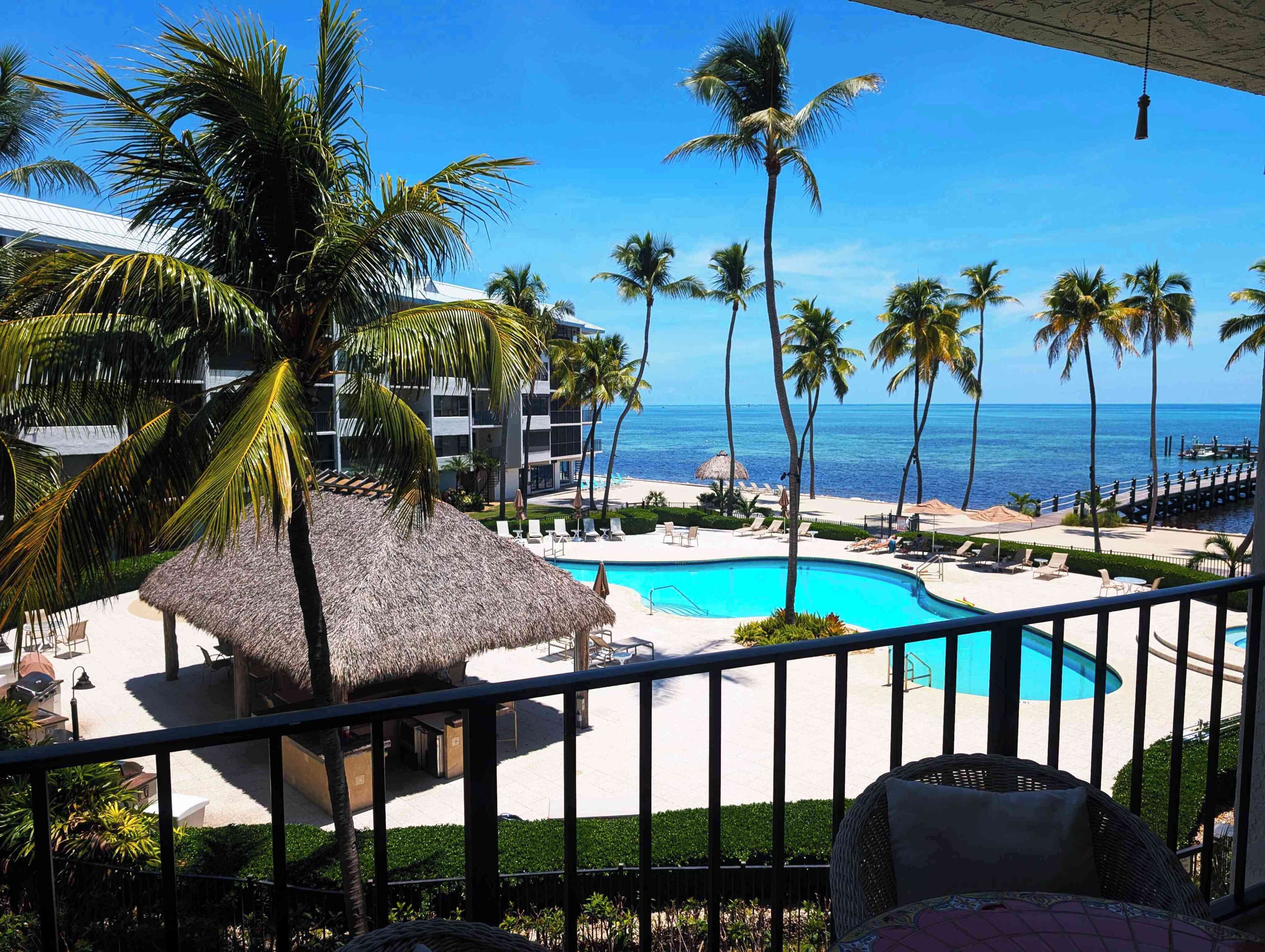 A pool area with a thatched-roof structure, lounge chairs, and a view of the ocean.