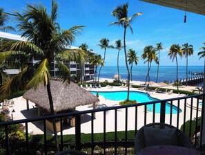 A pool area with a thatched-roof structure, lounge chairs, and a view of the ocean.