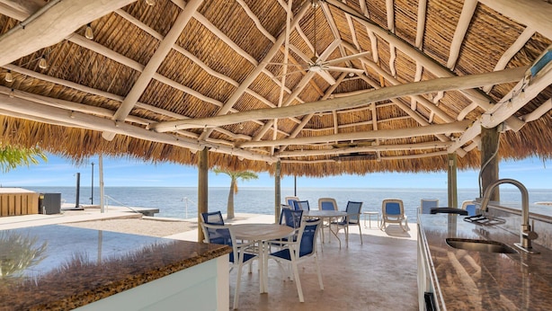 Une terrasse au bord de la plage, dotée d’un toit de chaume, de sièges extérieurs et offrant une vue sur la mer.