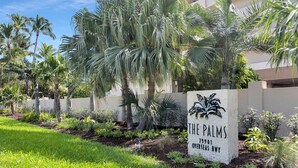 Une enseigne pour l’établissement « The Palms », avec en arrière-plan des palmiers et une pelouse bien entretenue.