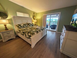 A bedroom with a bed, a nightstand, a dresser, a mirror, a window with a view, and a ceiling fan.