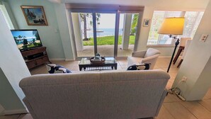 Ett vardagsrum med en soffa, ett soffbord, en tv och utsikt över stranden genom glasdörrar.