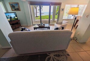 A living room with a sofa, a coffee table, a TV, and a view of the beach through glass doors. - Waterfront Home With Beautiful VIews (Islamorada)