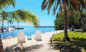 A beach with lounge chairs, a small table, and a clear view of the ocean. - Waterfront Home With Beautiful VIews (Islamorada)