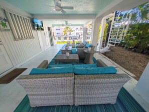 A covered outdoor seating area with wicker furniture and blue cushions, a ceiling fan, and a view of a residential building in the background. - Delightful vacation home located in the popular Islamorada neighborhood of Port Antigua. (Islamorada)