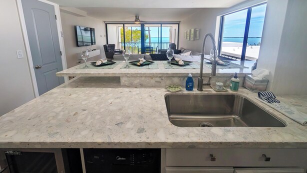 Una cocina moderna con una isla grande, lavavajillas integrado y vistas al océano a través de ventanas amplias.