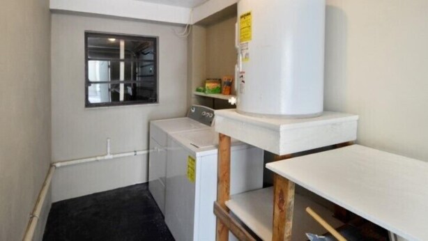 Un espace dédié à la lessive, comprenant un lave-linge, un sèche-linge et un grand objet cylindrique blanc posé sur une table en bois.