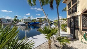 A marina with boats docked, palm trees, and a building with a balcony. - Beautiful updated stilted home makes for a super getaway. (Key Largo)