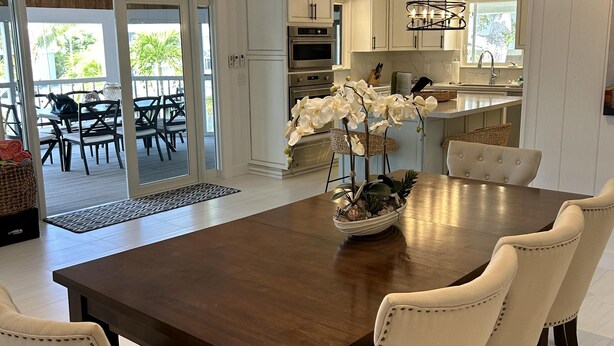 A spacious dining area with a wooden table and six upholstered chairs, a kitchen with white cabinets, and a view of the outdoor patio. - Beautiful updated stilted home makes for a super getaway. (Key Largo)