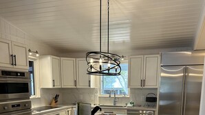 A modern kitchen with white cabinets, a large island with bar stools, stainless steel appliances, and a pendant light. - Beautiful updated stilted home makes for a super getaway. (Key Largo)