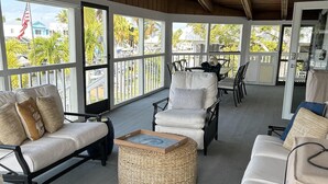 A covered outdoor seating area with wicker ottomans, white cushioned chairs, and a ceiling fan. - Beautiful updated stilted home makes for a super getaway. (Key Largo)