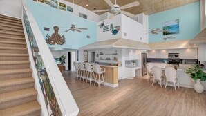 A spacious kitchen with a central island, a dining area with chairs, and a staircase with a railing.
