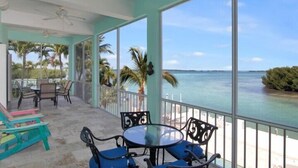 A balcony with a table and chairs, overlooking a body of water and palm trees.