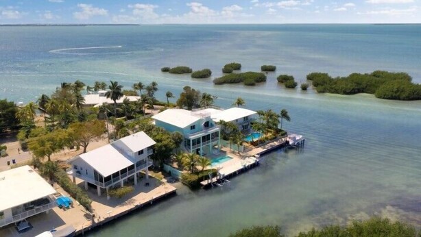 A coastal property with multiple buildings, a swimming pool, and a dock extending into the water.
