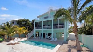 A two-story building with a swimming pool, outdoor seating, and palm trees.