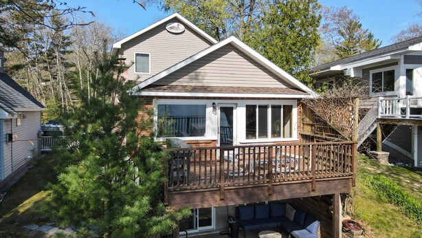 A two-story house with a deck, a covered patio, and a brick exterior. - Loons Landing - Relax on the lake, your perfect Traverse City retreat. (Traverse City)