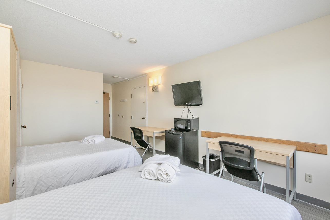 A hotel room with two beds, a desk, a chair, a television, and a trash bin.