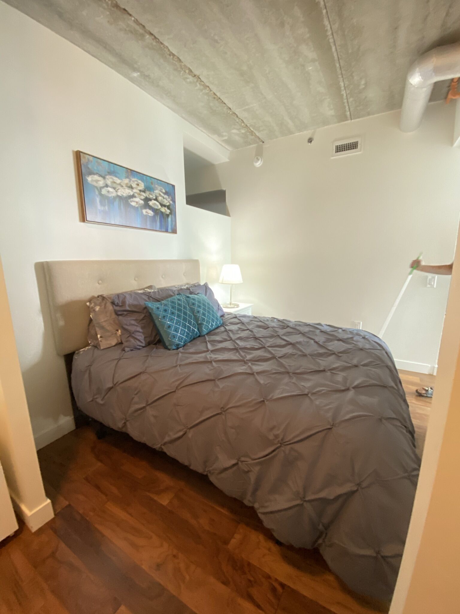 A bedroom with a bed, a nightstand, a lamp, and a painting on the wall.
