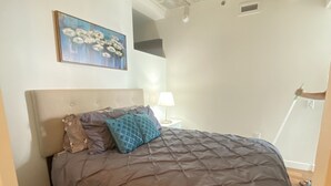 Une chambre à coucher avec un lit, une table de chevet, une lampe et un tableau au mur.