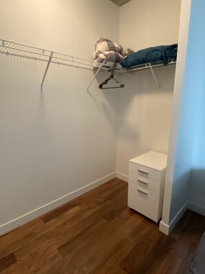 Un vestidor pequeño con una estantería metálica, un aparador blanco y una falda para cama azul.