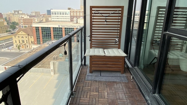Un balcon avec un banc en bois, une rambarde en métal et une vue sur le paysage urbain.