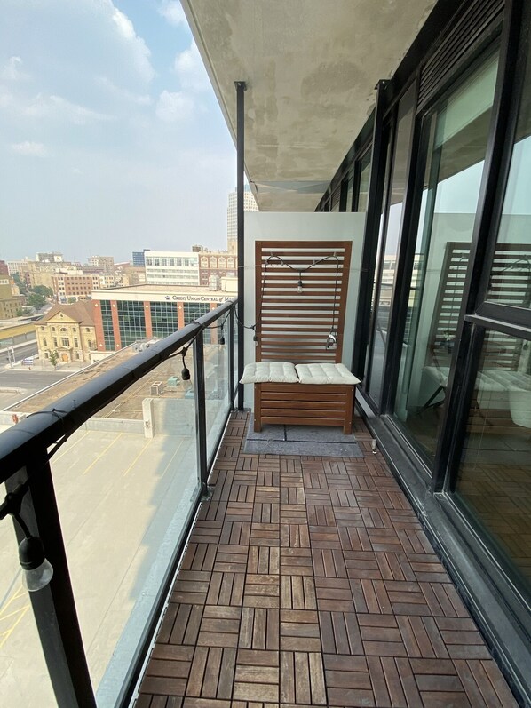 Un balcón con banca de madera, barandilla metálica y vista a un paisaje urbano.