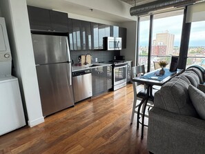 Una cocina moderna con electrodomésticos de acero inoxidable, un comedor con mesa y sillas, y un amplio ventanal con vistas a la ciudad.