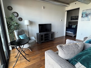 A living room with a sofa, a chair, a TV stand, and a floor lamp. - Downtown luxury 1 bedroom wifi and laundry across arenas (Winnipeg)