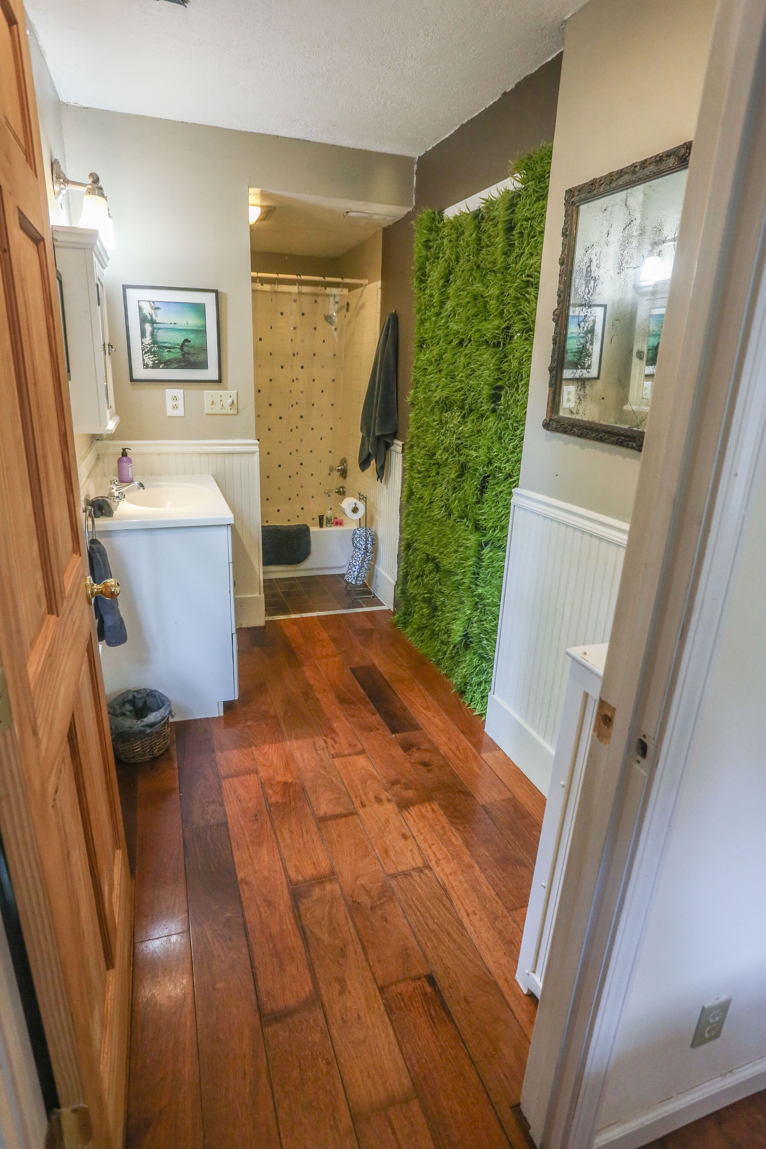 A narrow hallway with wooden flooring, a white sink, and a green vertical garden wall.