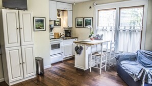 Eine kleine Küche mit weißen Schränken, einem Herd und einer Spüle. Es gibt eine Essecke mit Tisch und Stühlen und ein Sofa im Wohnzimmer.