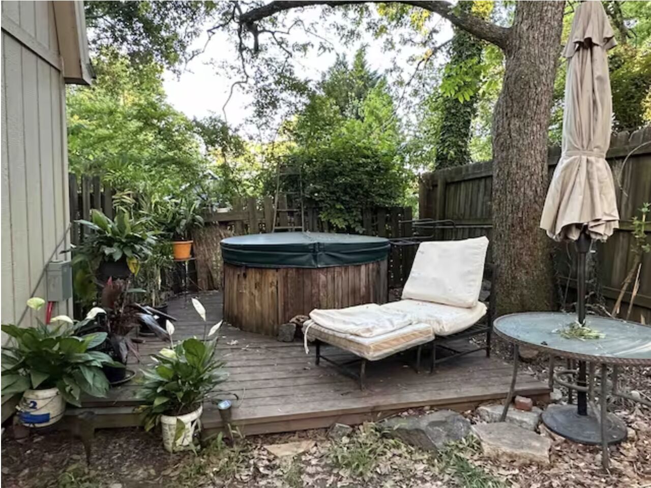 A wooden deck with a hot tub, a lounge chair, and a table with an umbrella.